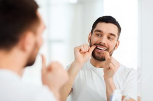 'man flossing teeth in mirror'