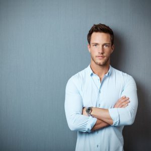 'man with crossed shoulders in front of blue background'